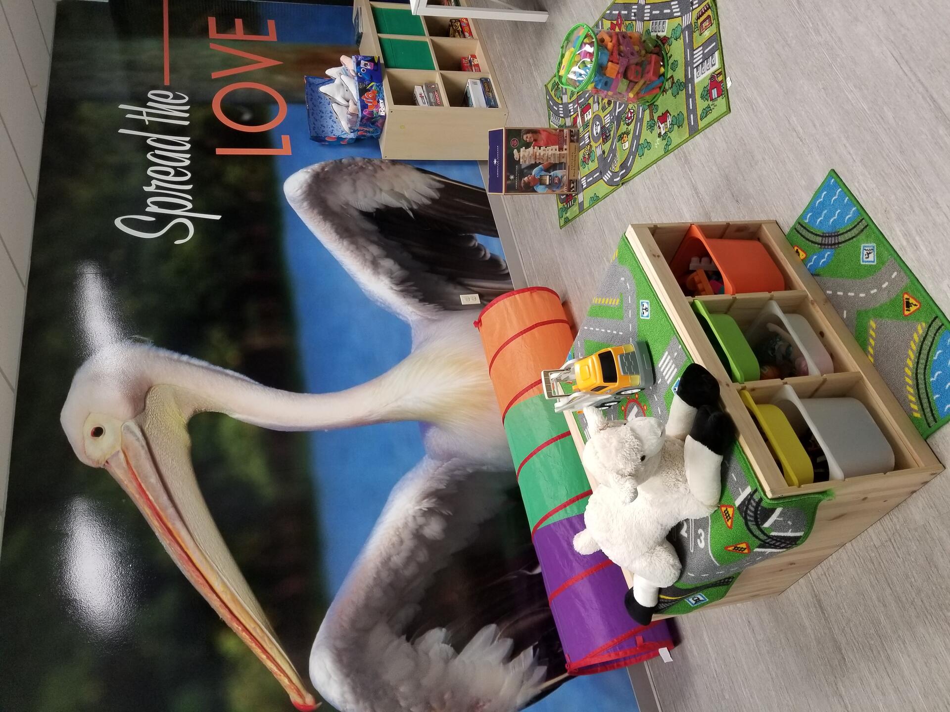 Rufus Room — visitation space with play tunnels and toys under the "Spread the Love" pelican mural